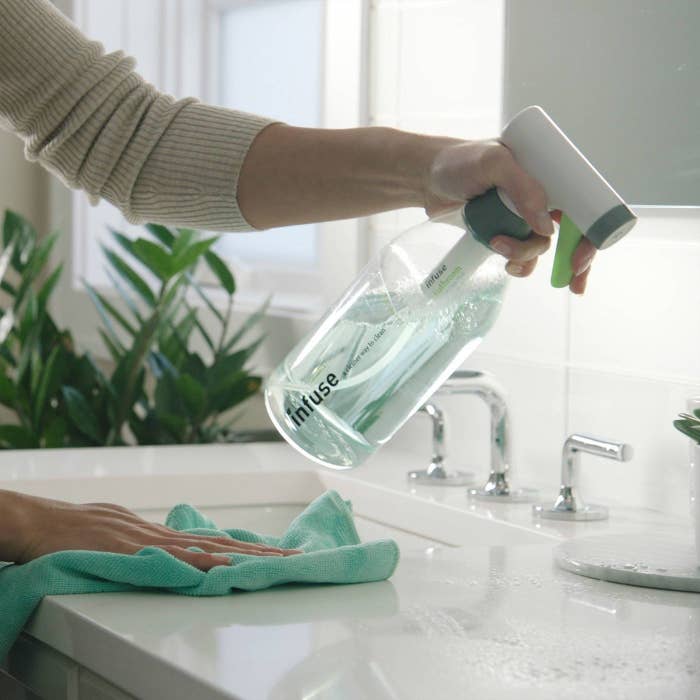 a model using the spray bottle of infuse cleaner to clean their bathroom counter