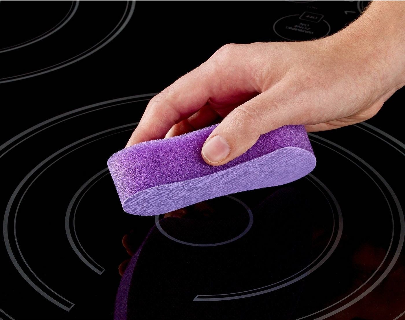 a model using a purple sponge to clean a stovetop