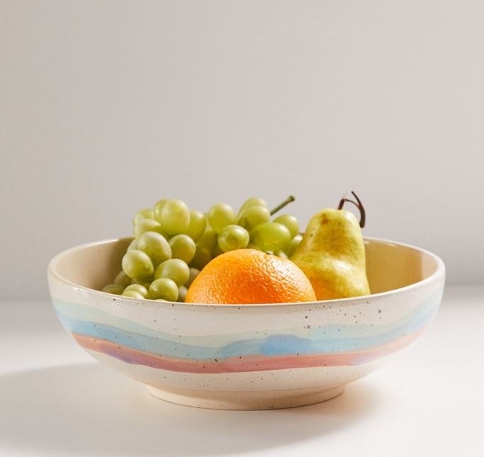 An oval bowl with a watercolor-style paint in blue and red around the outside with fruit in it