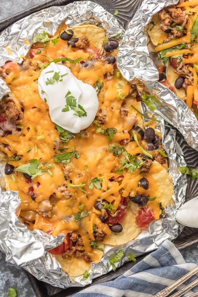 Nachos topped with ground meat, black beans, tomato, herbs, and cheese in foil packets.