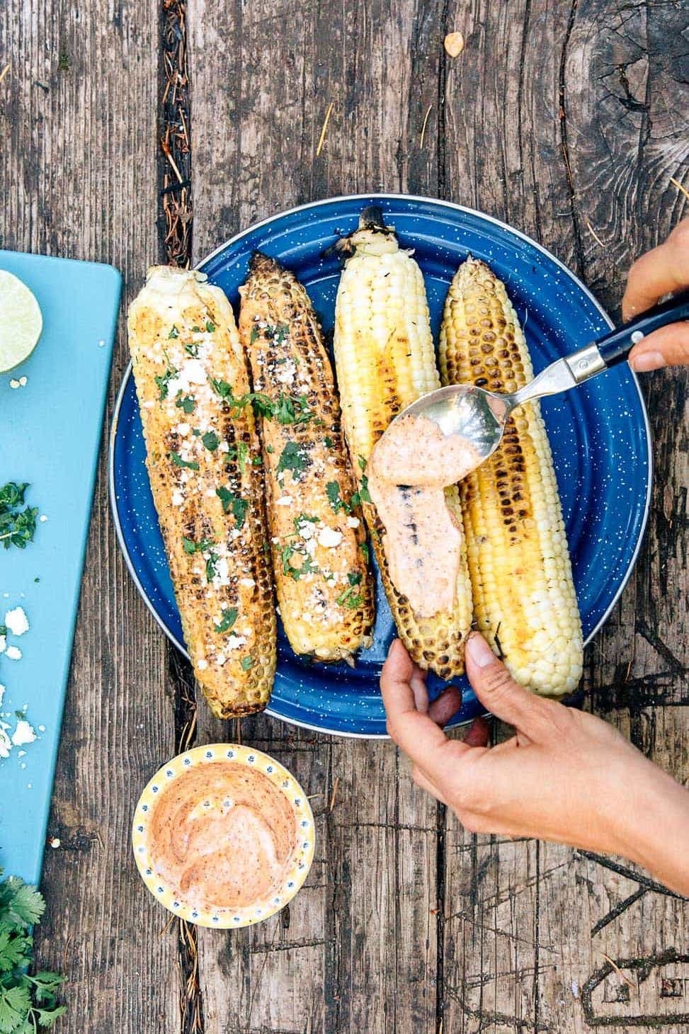 Someone brushing grilled corn with a spicy mayo and chili powder mixture to make Mexican street corn.