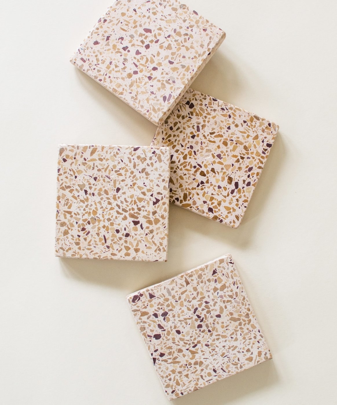 Four square coasters made of terrazzo stone in tan with specks of browns all over them