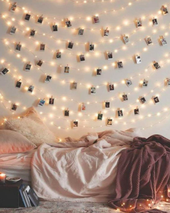 A set of photo clip string lights with Polaroid photographs above a bed 