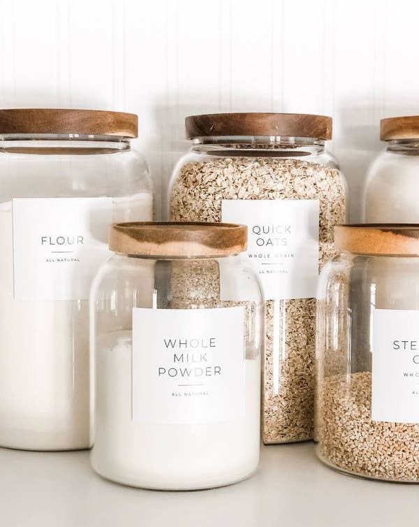 Assorted glass jars with square white labels ion the front saying what's inside the jar including "Whole Milk Powder" and "Flour"