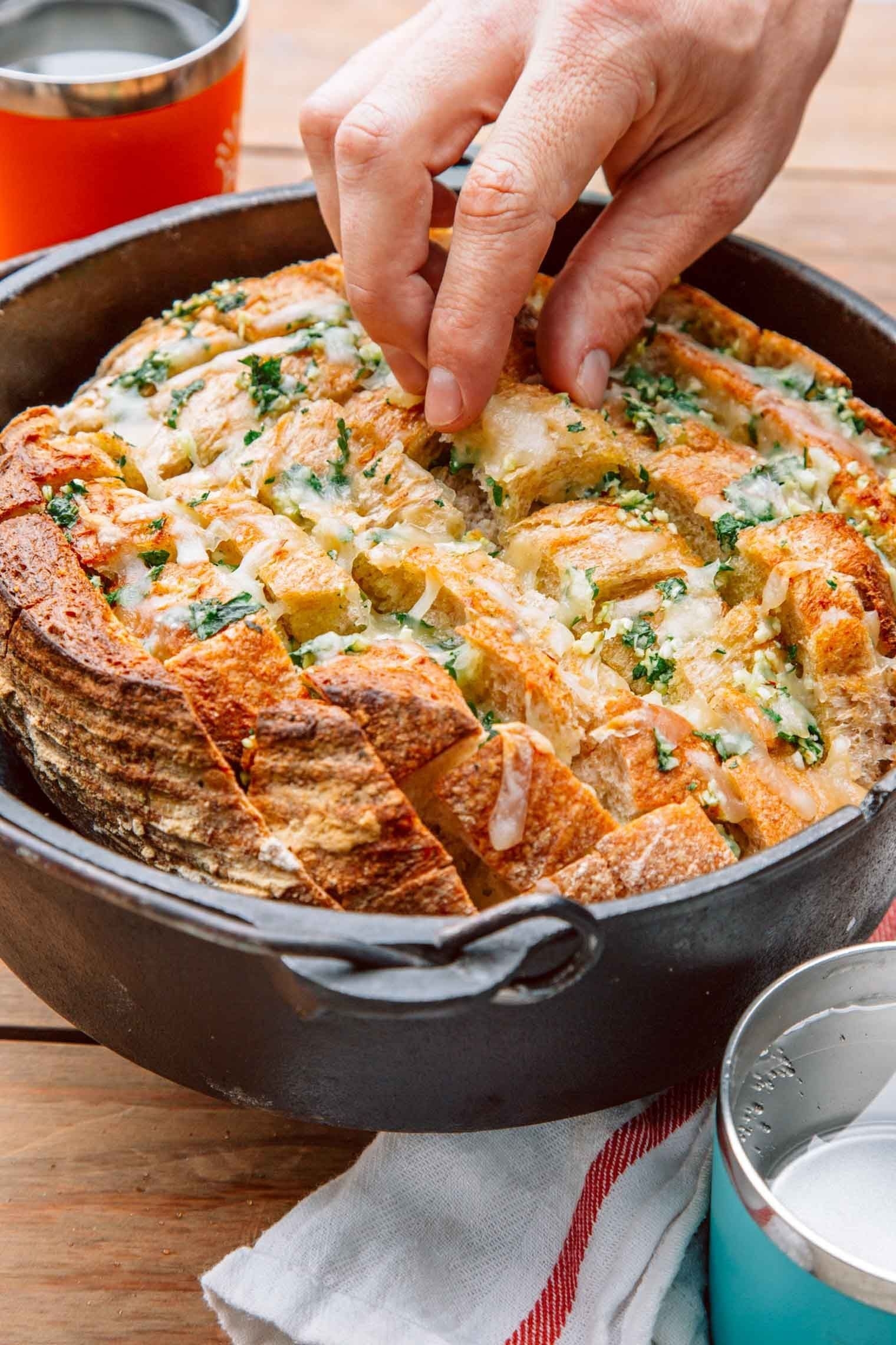Hands reaching into a cast iron skillet full of pull-apart garlic bread.