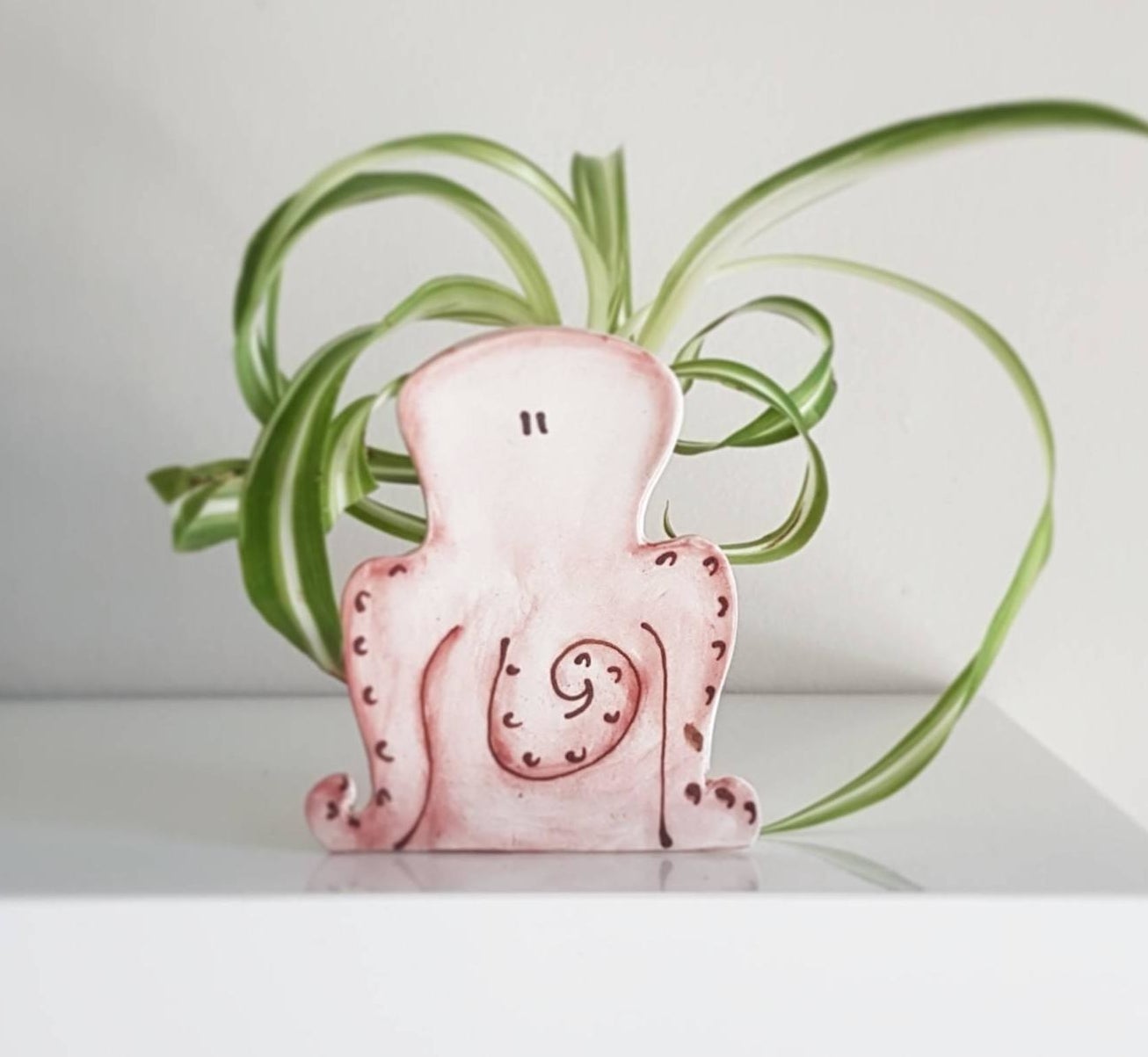 The small planter in red that looks like an octopus and has a green air plant in it