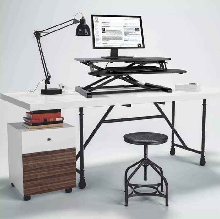 A black standing desk with a keyboard and monitor atop it