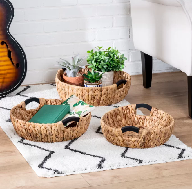 Three brown woven baskets filled with plants and notebooks on a white and black rug.