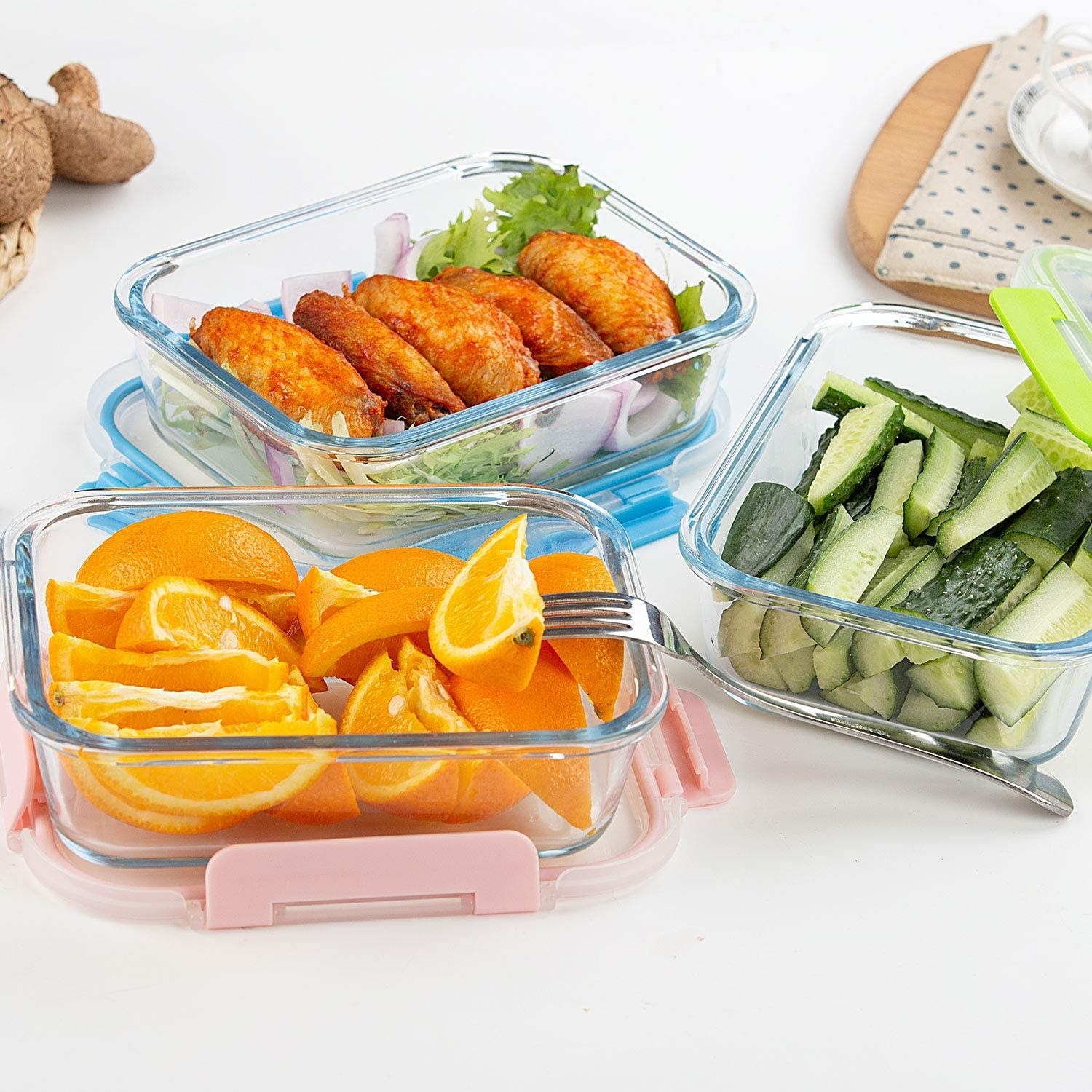 Three meal prep containers holding orange slices, cucumber slices, and chicken wings