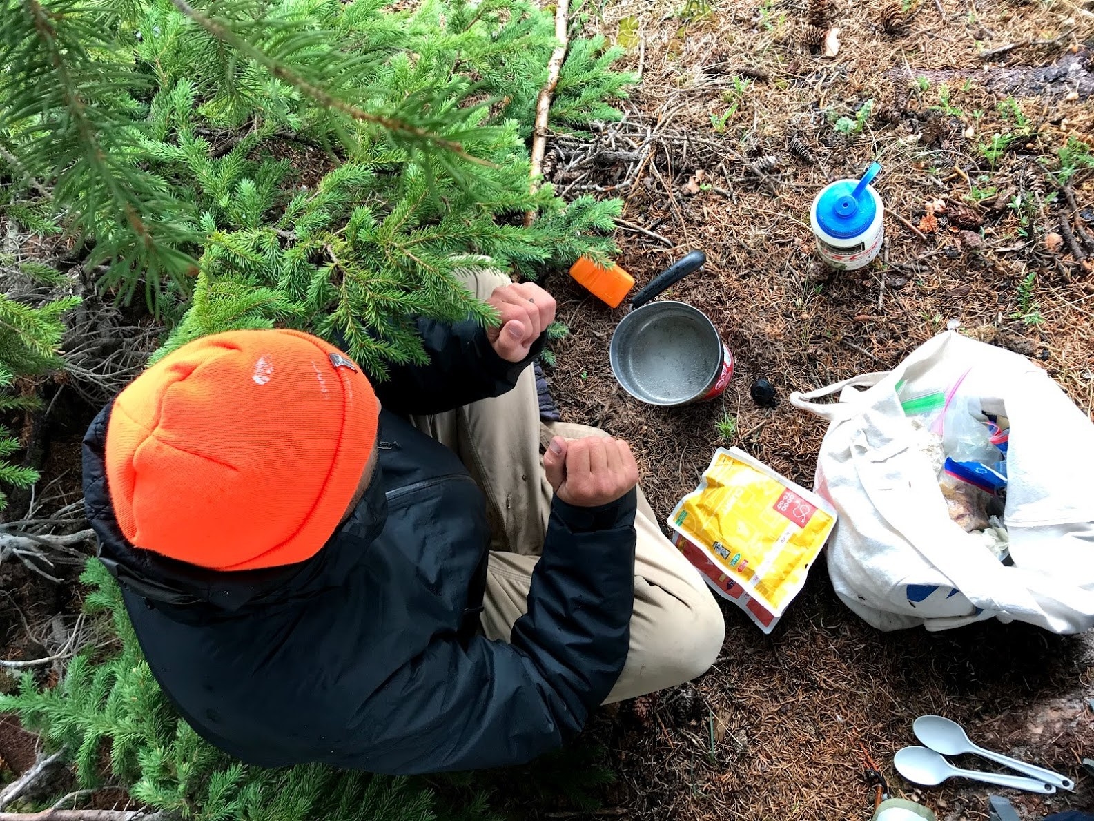 bird&#x27;s eye view of a person sitting outside on the ground preparing to cook dinner on a small camping stove