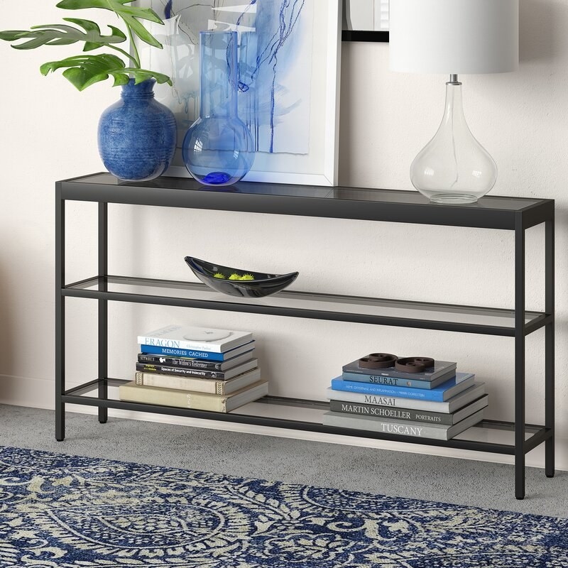 A long black metal console table with three glass shelves