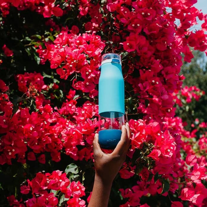 A person holding a water bottle against a wall of flowers