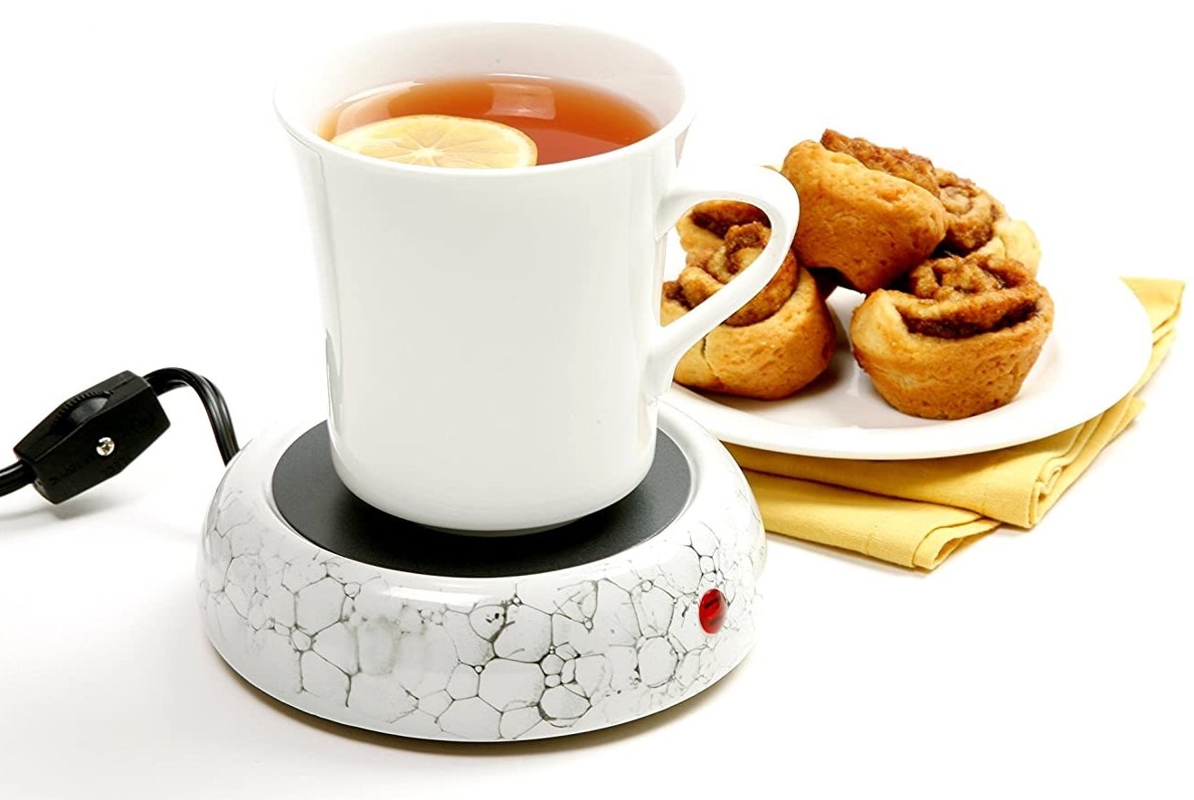 A mug filled with tea sitting on a circular electronic mug warmer. 