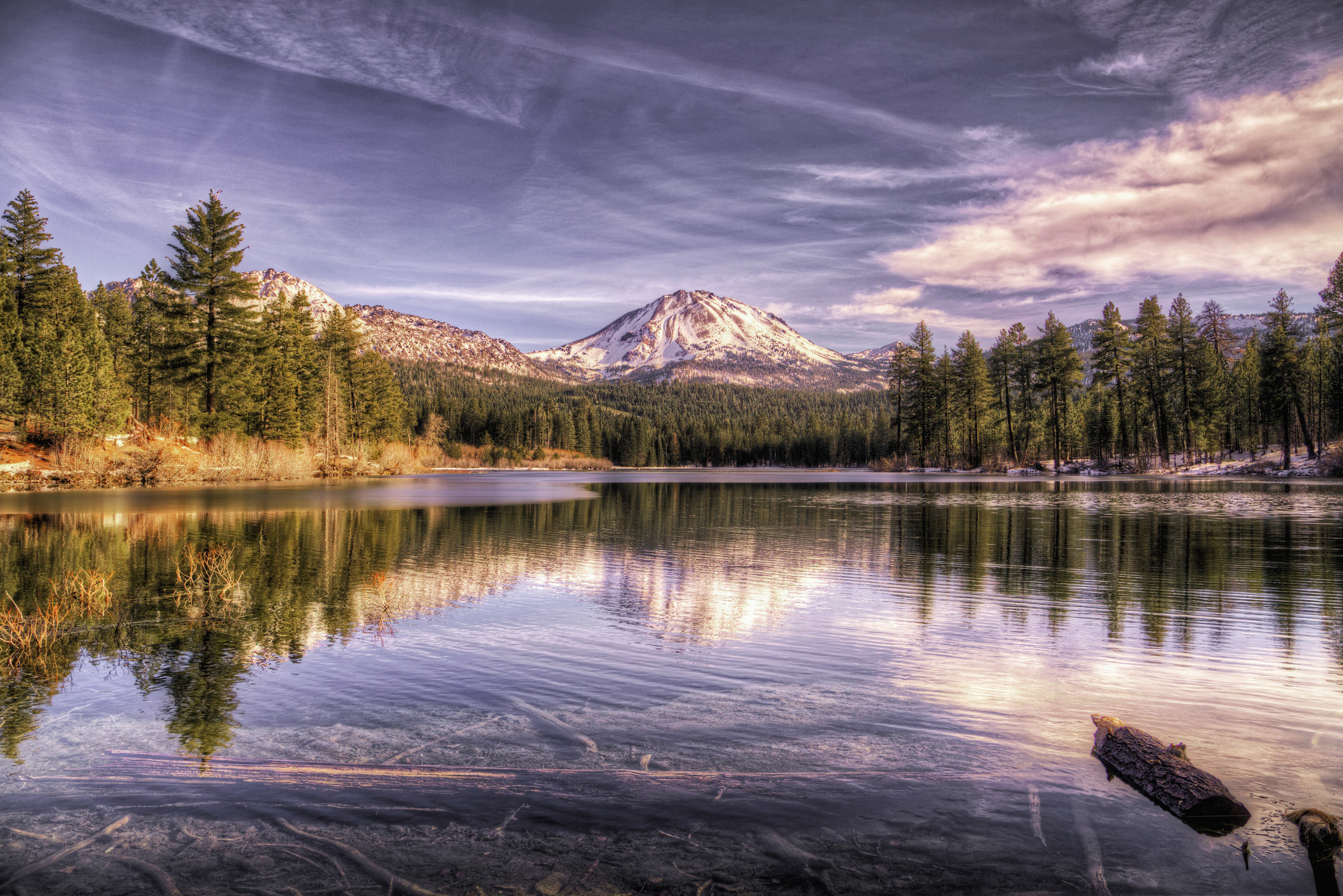 雪山山峰和一个玻璃状湖，在拉森火山国家公园（Lassen Volcanic National Park）包围着树木。