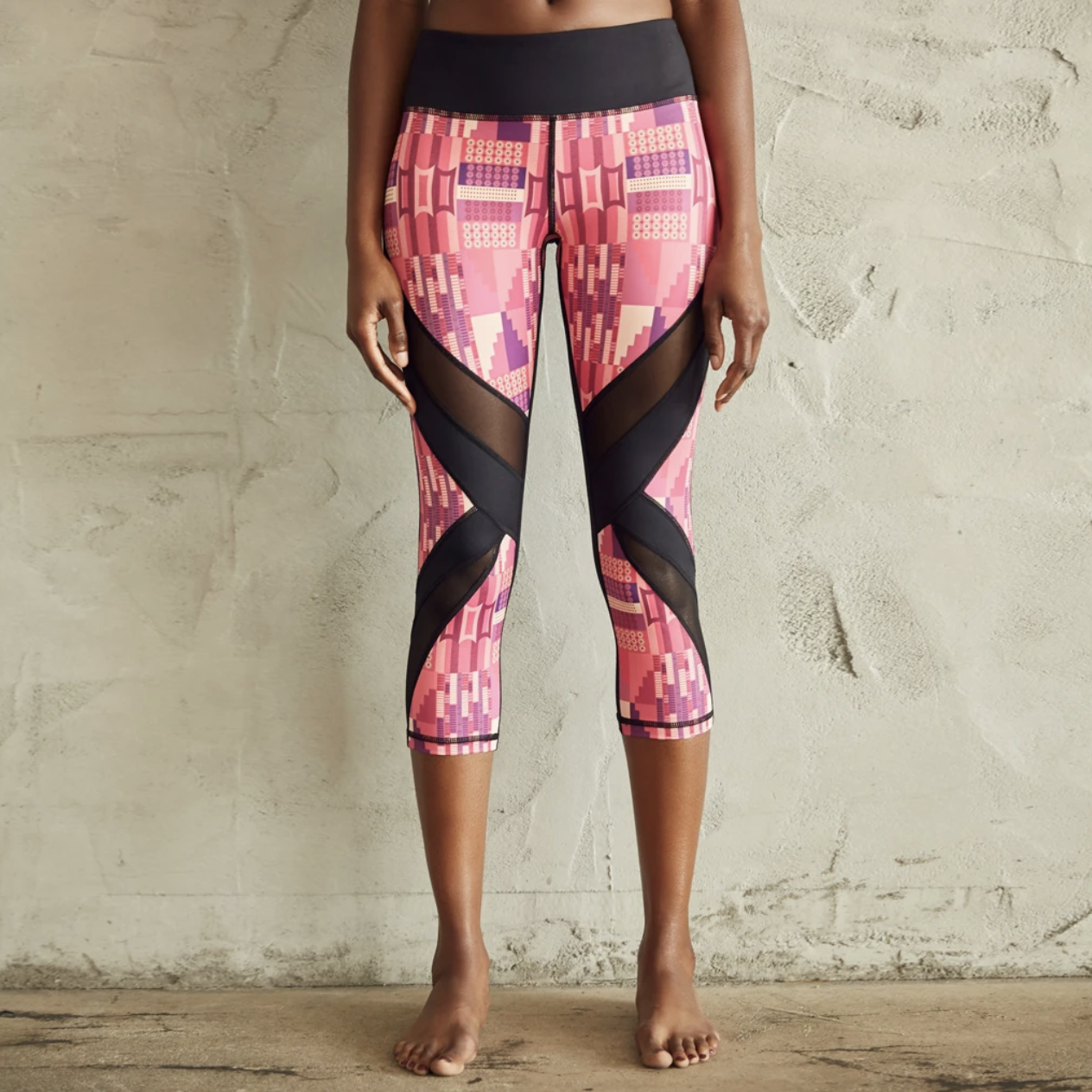 A model in pink West African-inspired print leggings with diagonal black mesh panels at the knees 