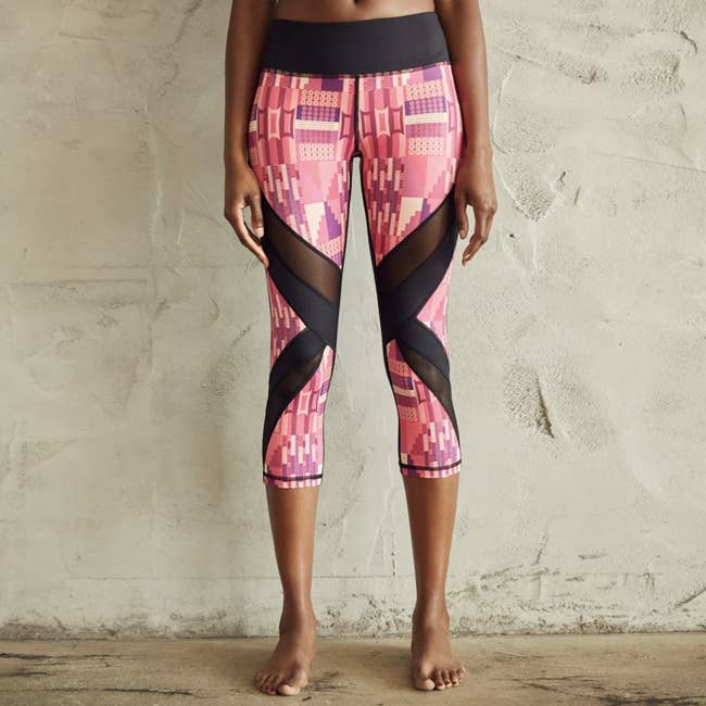 A model in pink West African-inspired print leggings with diagonal black mesh panels at the knees 