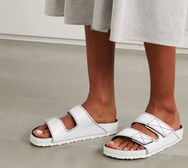 A model wearing the Proenza Schouler + Birkenstock Arizona topstitched glossed-leather sandals in white.