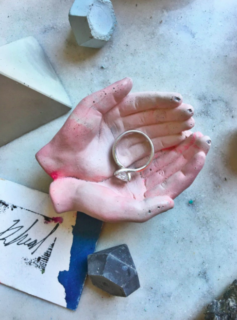 A pink hand-shaped catch-all tray holding an engagement ring