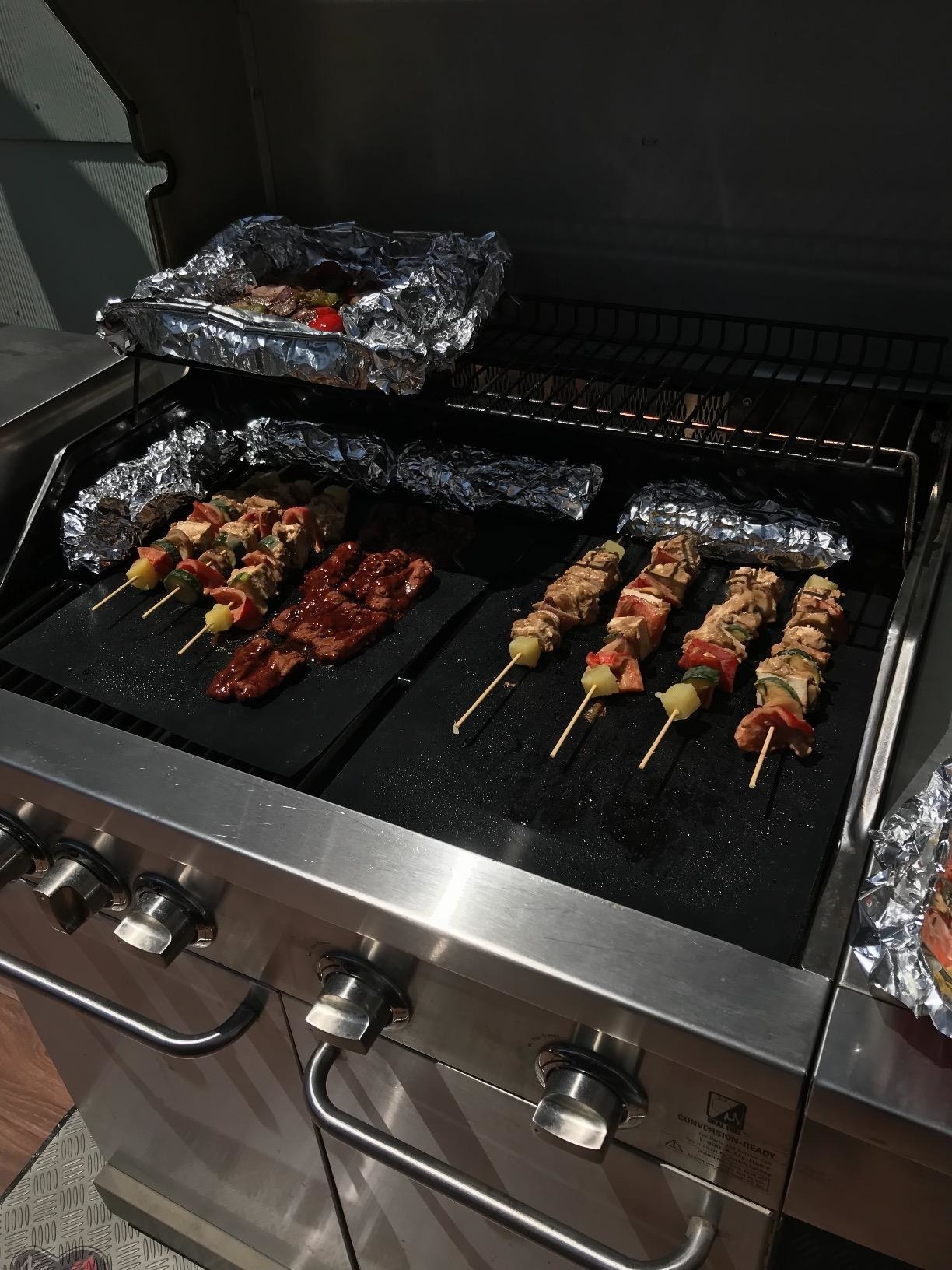 Two black grill mats with kabobs sitting atop them