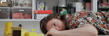 A gif of Lena Dunham laying beside a miniature living room set in her film, Tiny Furniture 