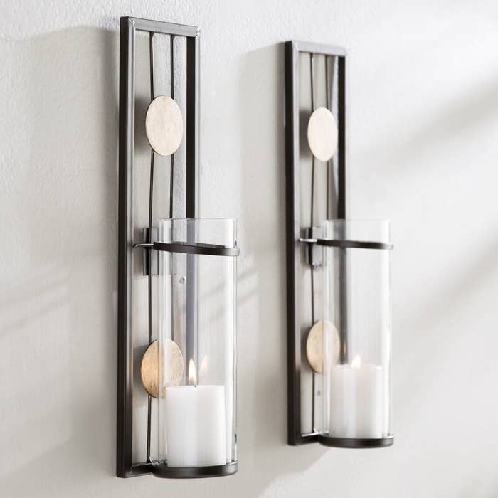 The sconces with metal rectangular backs accented with two brushed-gold circles, and a glass space for candles
