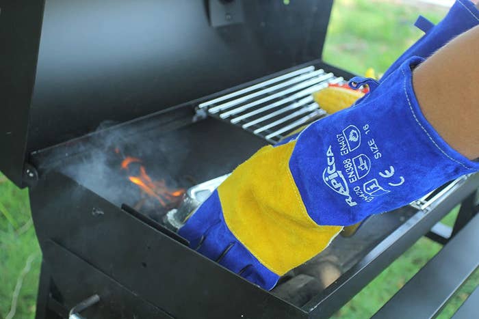 A model wearing a pair of long blue and yellow leather gloves while cooking on a grill
