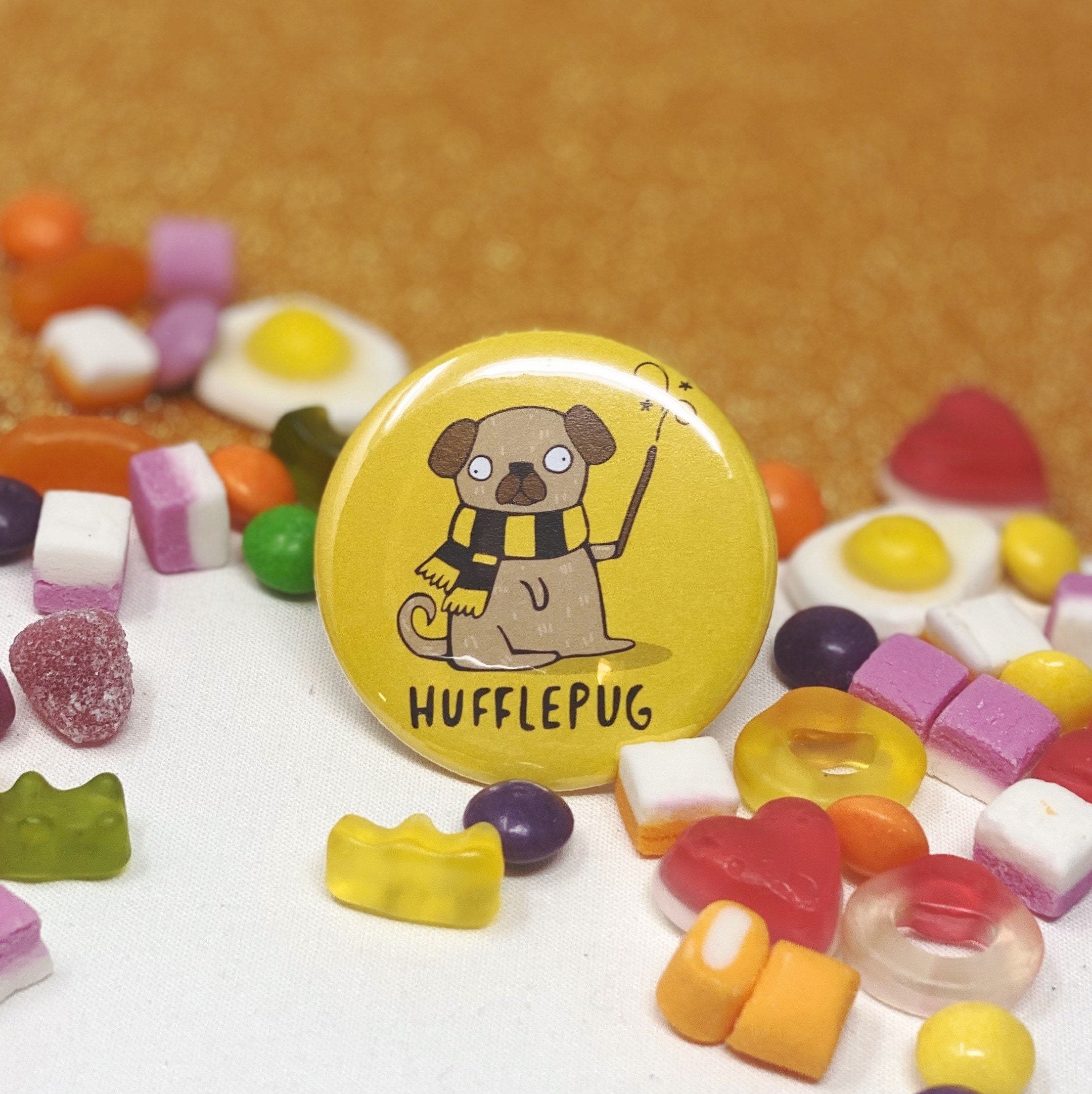 a yellow button pin with a pug on it wearing a yellow and black scarf and holding a wand with the words &quot;hufflepug&quot; written under it
