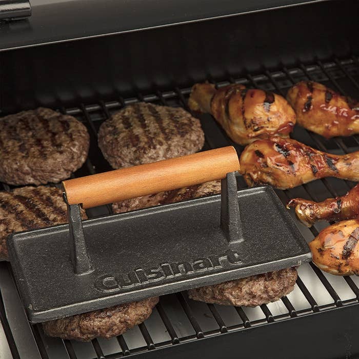 A dark-gray metal grill press the length of two hamburgers with the Cuisinart logo prominently featured