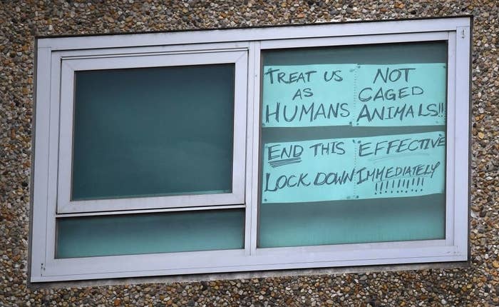 A public housing window with a note saying "Treat us as humans, not caged animals! End this effective lockdown immediately!"