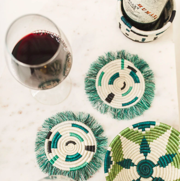 Two green fringe coasters next to a bottle of wine