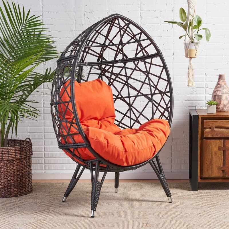 A teardrop-shaped egg chair with orange cushions and four legs