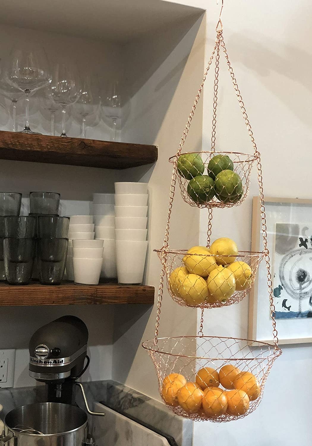 Three-tiered hanging basket displayed in a kitchen holding three different types of fruit in each basket