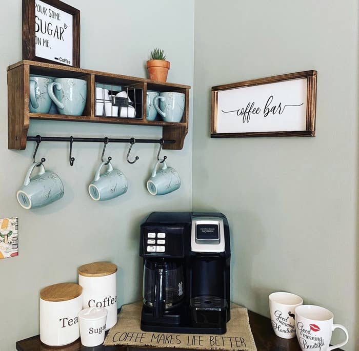 Reviewer image wooden shelf with three compartments holding mugs and K-cups, plus a bar with hooks for additional mug storage