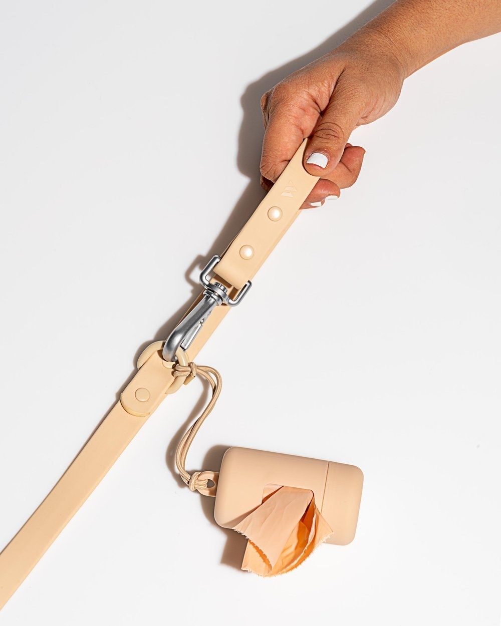 A peach-colored dog poop bag carrier connected to a leash.