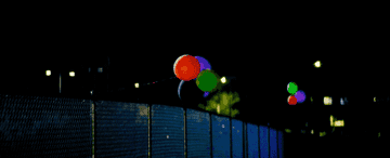 Red, green, purple, and black balloons blowing in a breeze.
