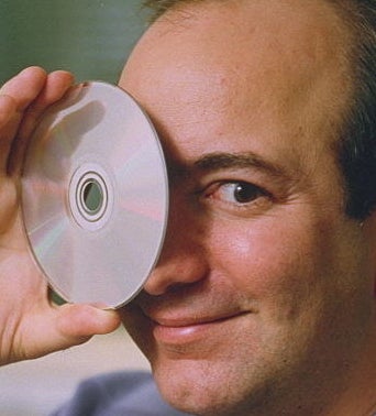 A closeup of Jeff Bezos holding a CD to his eye