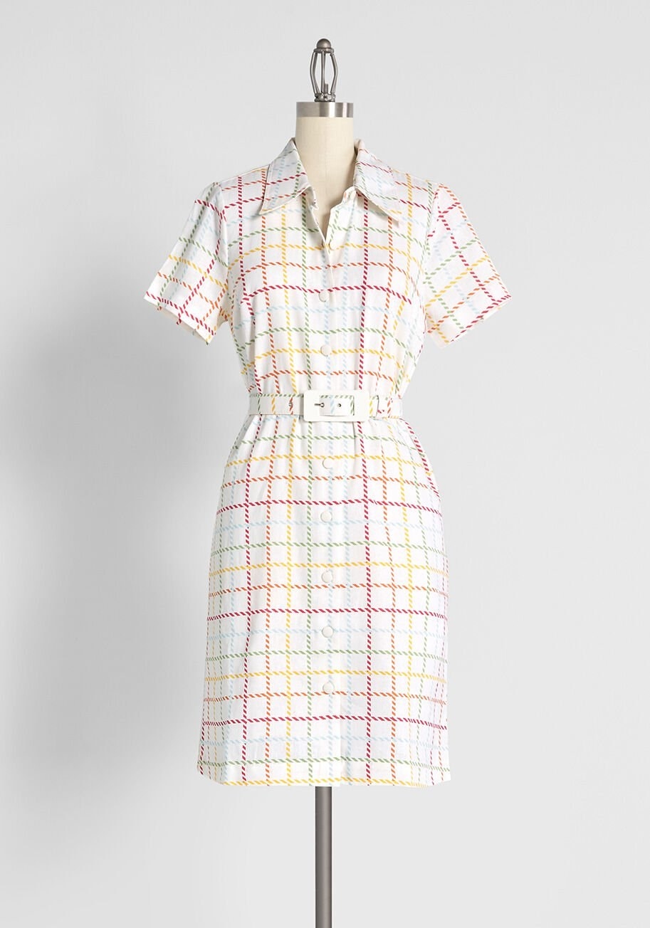 white shirtdress with multicolored checked stripes, buttons down the front, and a belt