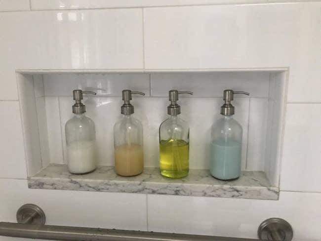 A reviewer photo of four soap dispensers in a shower filled with different liquids 