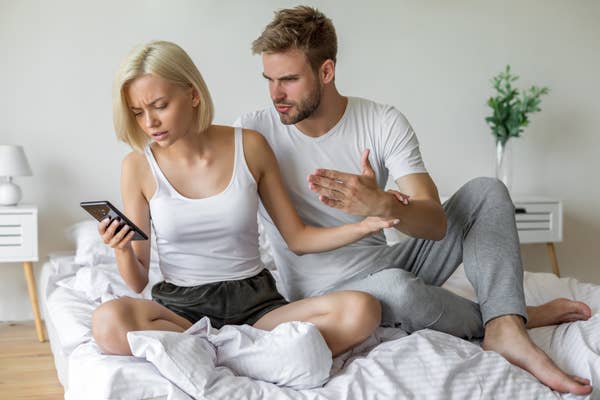Photo of a couple arguing over a phone in bed