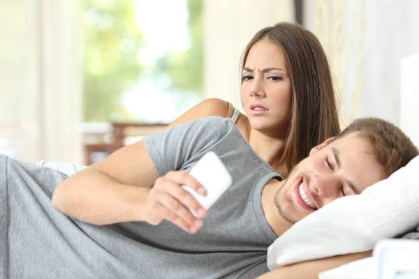 Photo of a couple in bed, with the woman peering over at her boyfriend's phone