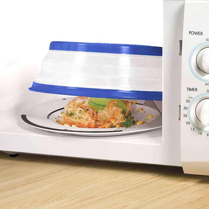A large silicone bowl is covering a plate of food in the microwave