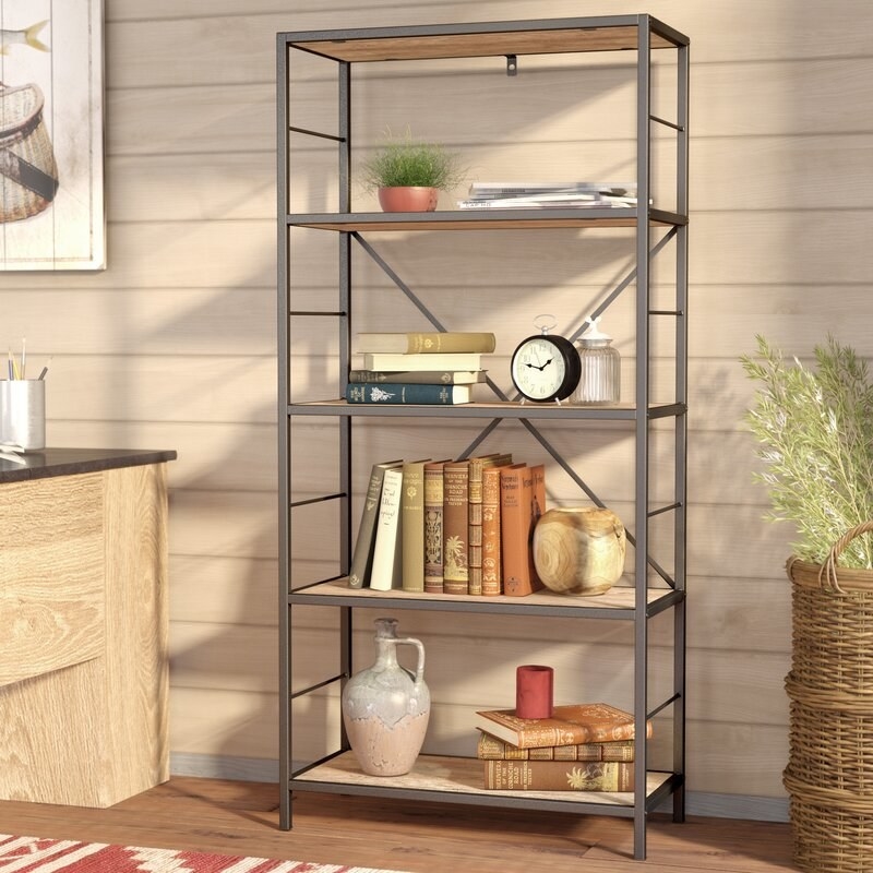A four-shelf bookcase with wood shelves and iron base with books and other trinkets on it