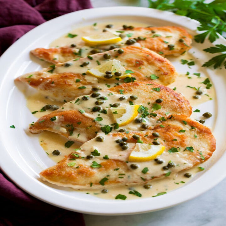 A plate of chicken piccata with capers in a lemon sauce.