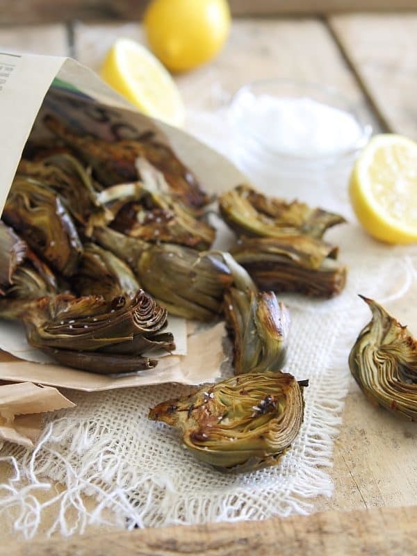 Crispy baby artichokes on a tabletop with lemon wedges.