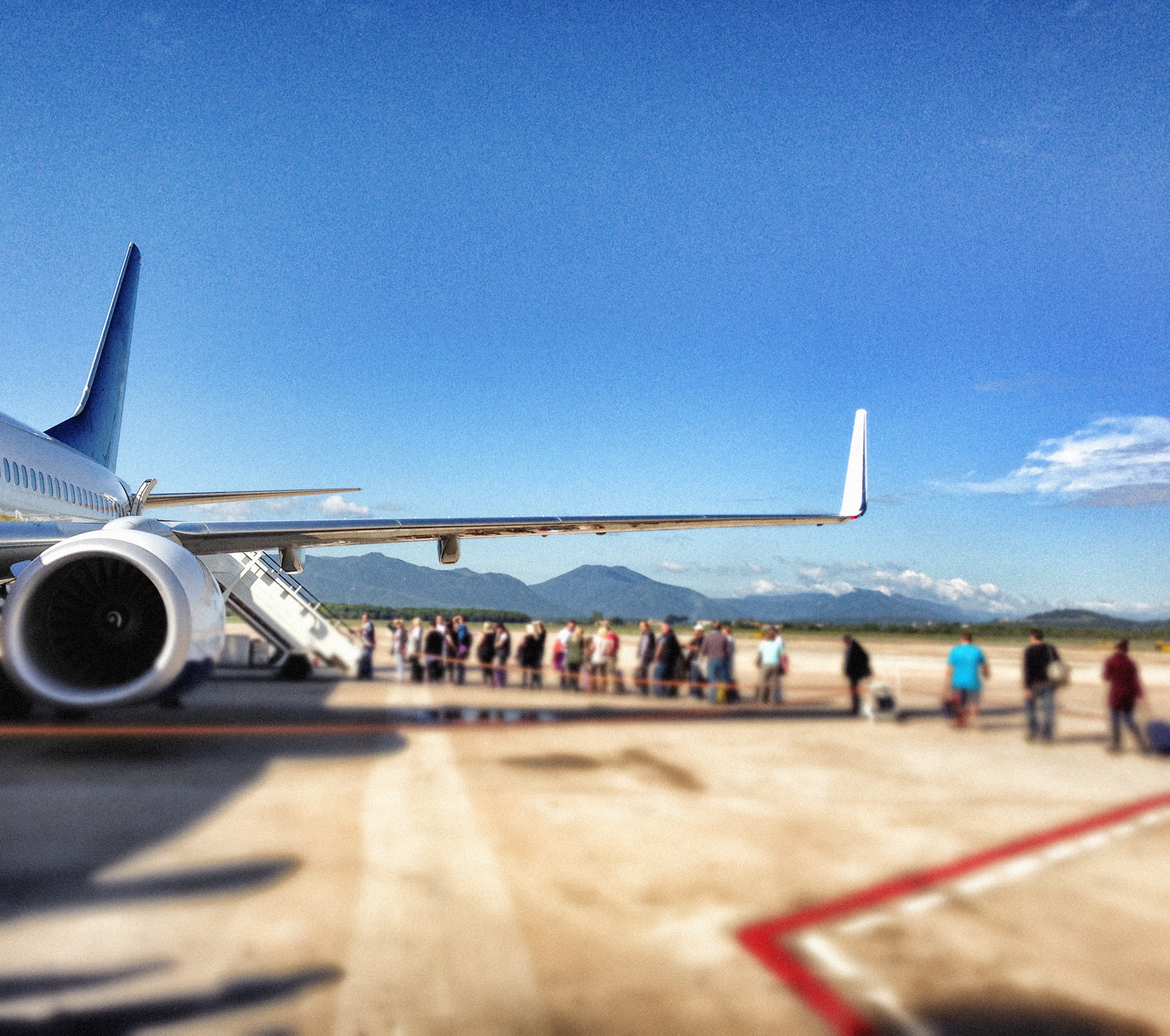 an airplane waiting on the tarmac, mountains in the distance, passengers queuing to board