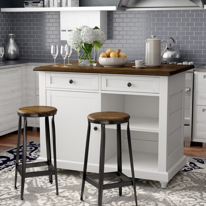 The white island with brown countertop and drawers and a cupboard and a recessed space with a shelf for storage