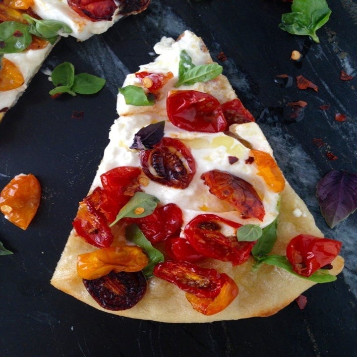 A slice of pizza with roasted tomatoes, mozzarella cheese, and shredded basil.
