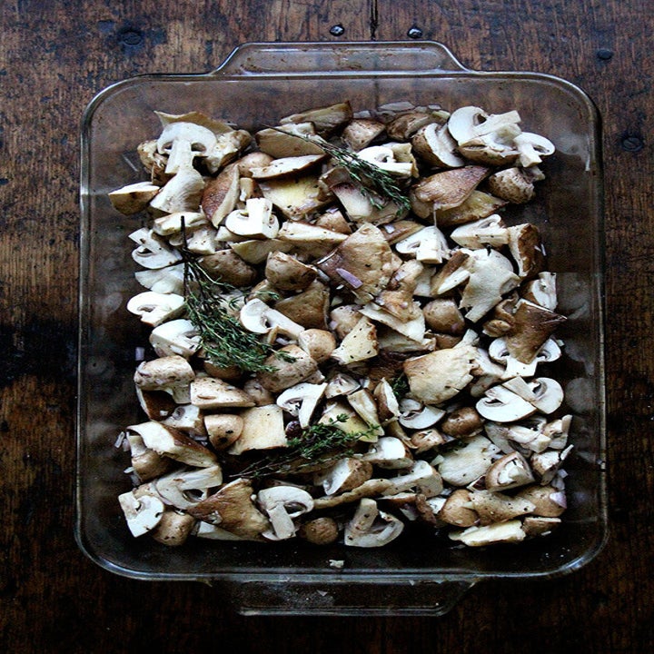 A glass baking pan filled with sliced mushrooms and thyme.