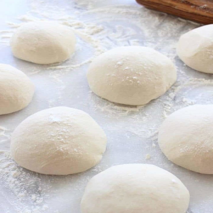 Seven little rounds of pizza dough on a floured surface.