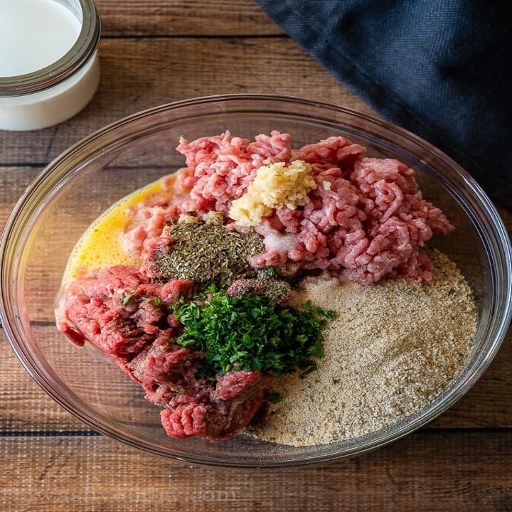 Ingredients for meatballs in a mixing bowl including bread crumbs, ground meat, egg, and spices.